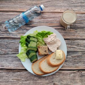 Zdjęcie przedstawia Dietę podstawową:  Jogurt typu islandzkiego naturalny Skyr Chleb mieszany pszenno-żytni Masło extra Pasztet wieprzowy z żurawiną Twarożek pomidorowy Ogórek świeży Sałata zielona Kawa zbożowa z mlekiem Woda mineralna